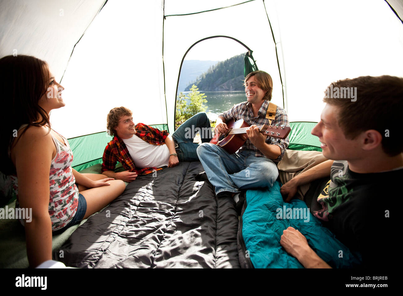 Les jeunes adultes camping écouter à un ami jouer de la guitare à l'intérieur de la tente à côté d'un lac dans l'Idaho. Banque D'Images