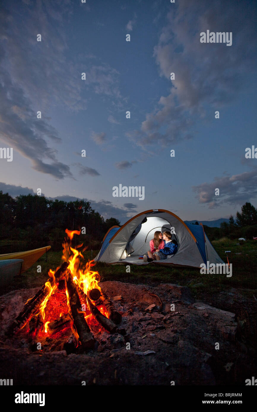 Young adult couple camping avec un feu de camp et les kayaks sur une belle soirée d'été. Banque D'Images