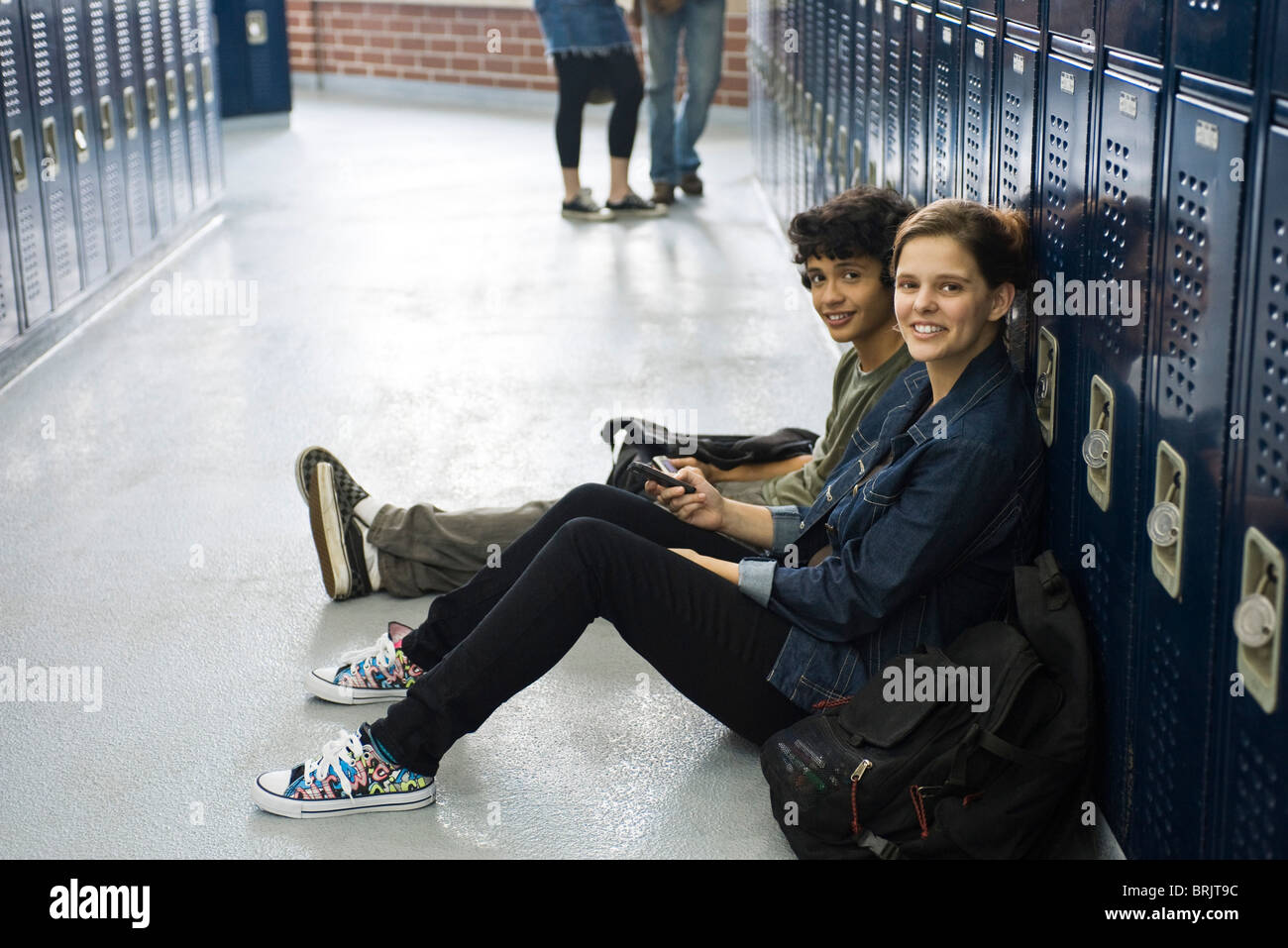 High school student sitting on floor with friend par casiers dans le couloir de l'école Banque D'Images