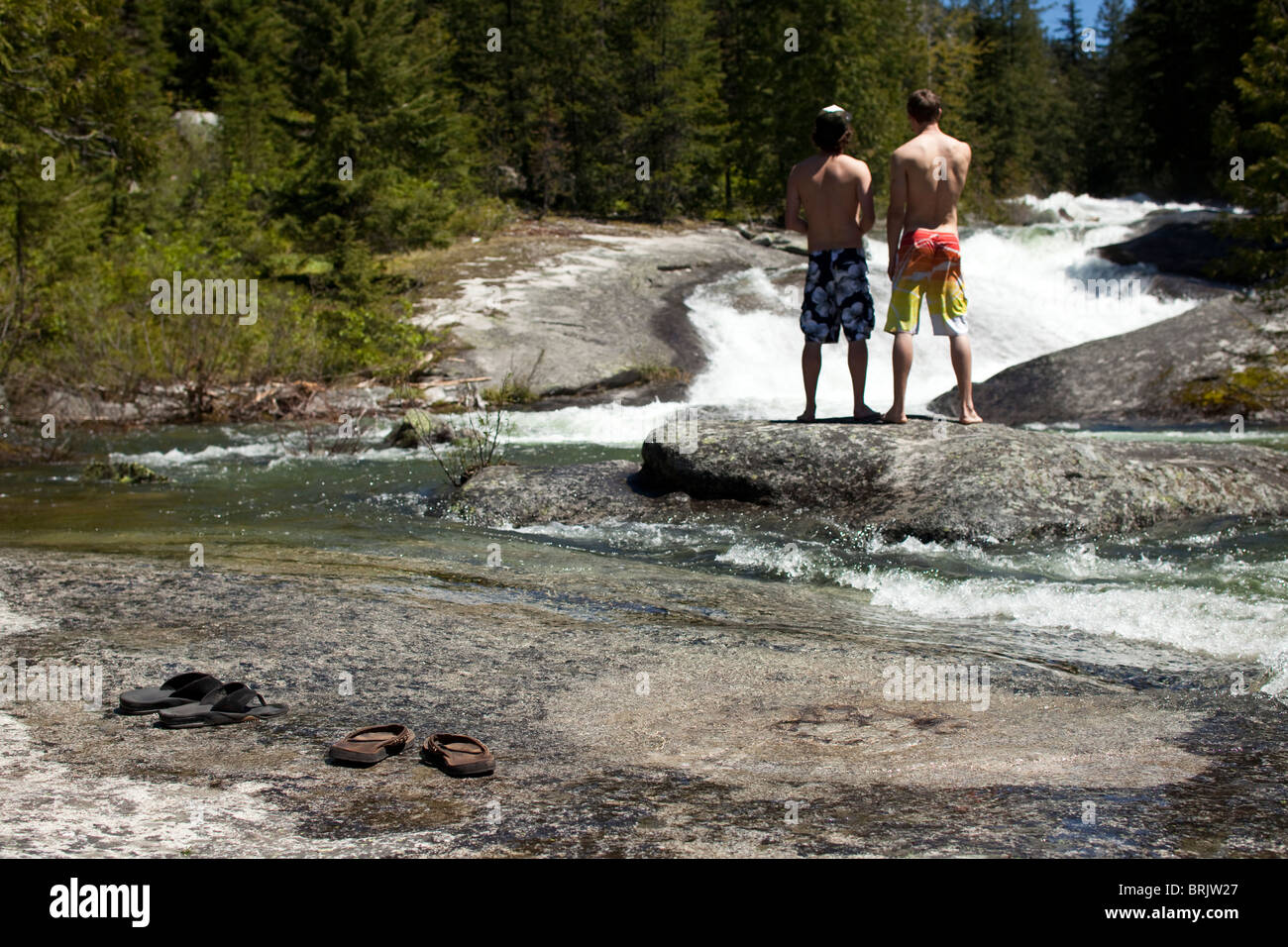 Deux jeunes hommes se tenant debout sur une petite île parle de sauter dans la rivière de congélation. Banque D'Images