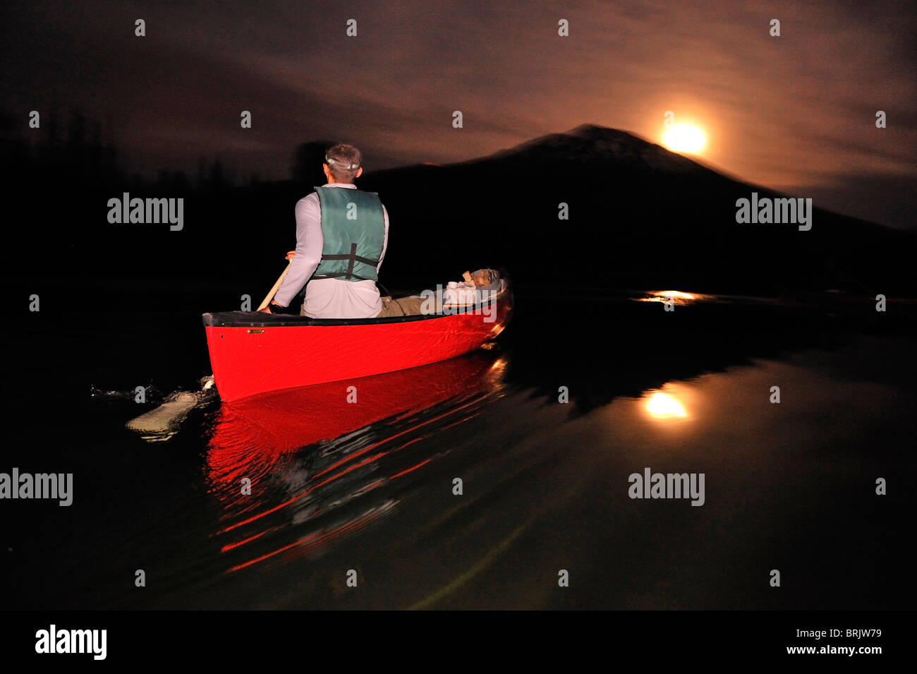 Un homme canoë dans un bateau rouge dans la nuit sur un lac de montagne dans l'Oregon. Banque D'Images