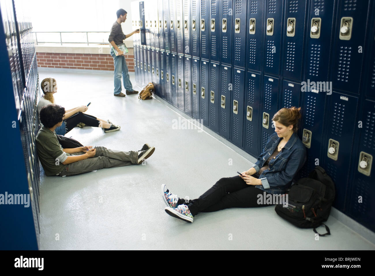 High school students sitting on floor casiers par l'utilisation de téléphones cellulaires Banque D'Images