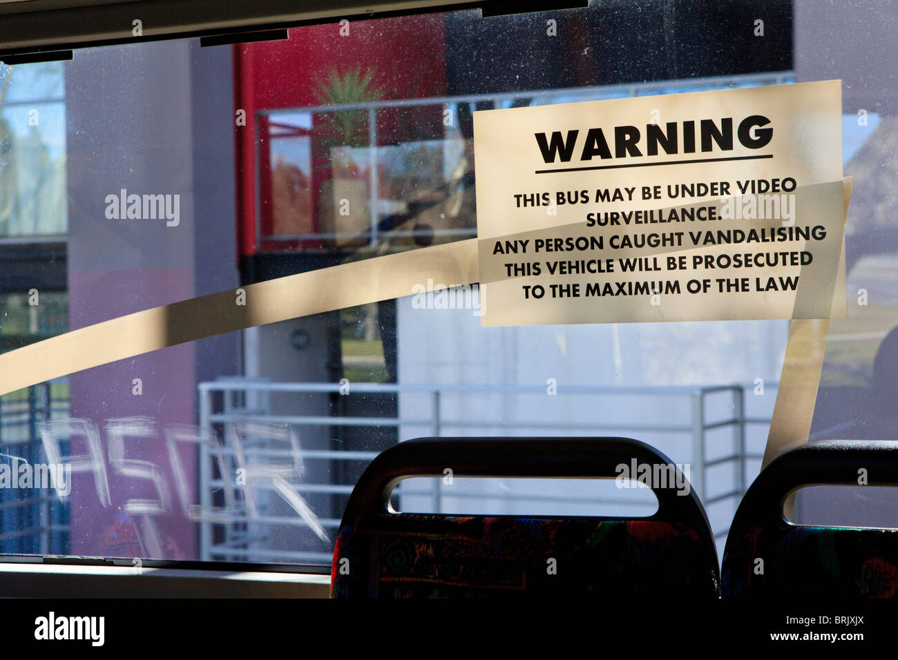 Surveillance vidéo avertissement que tous les actes de vandalisme seront poursuivis à côté de l'écriture graffiti rayé dans la fenêtre de l'autobus Banque D'Images