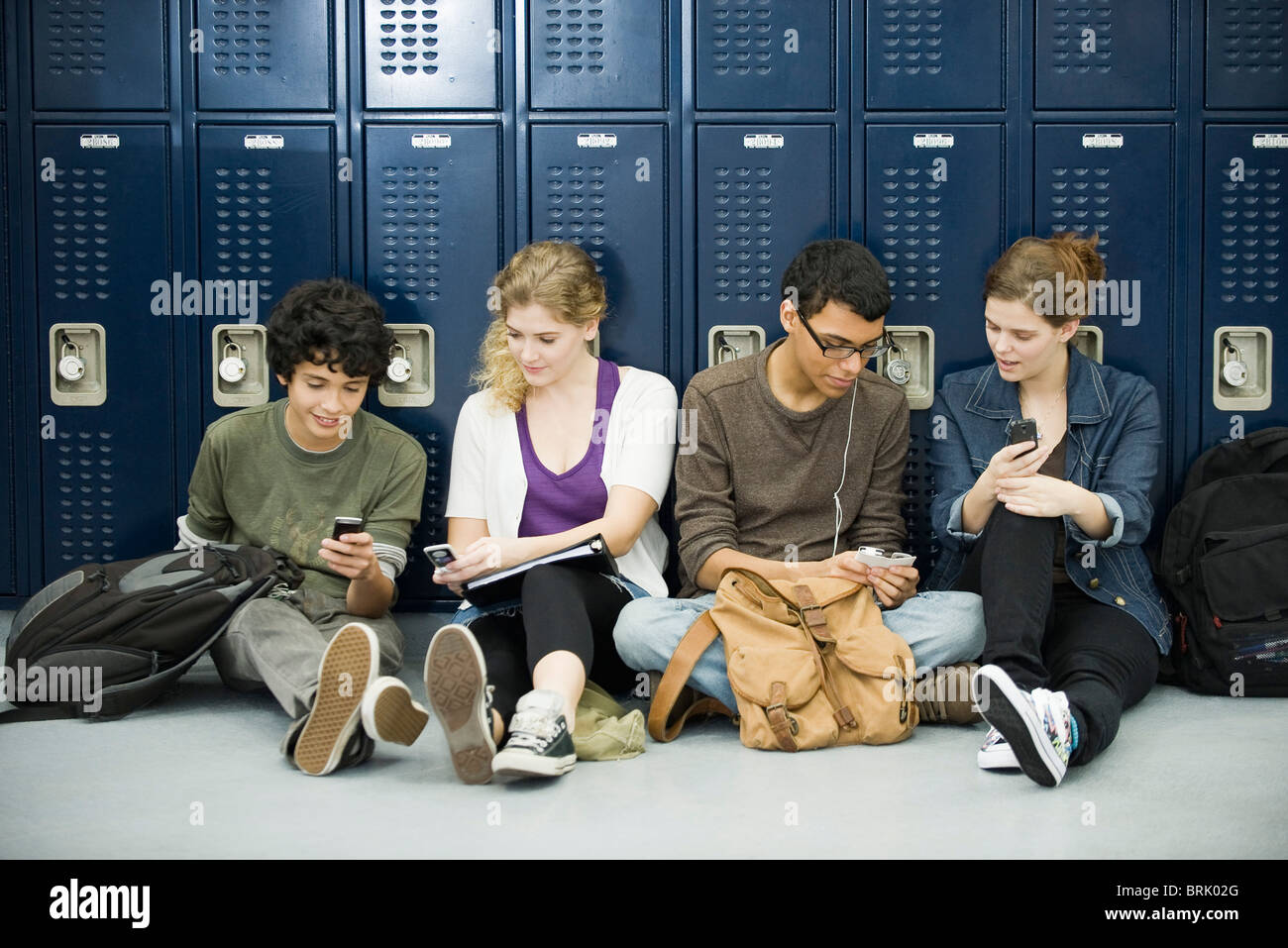 Les élèves du secondaire à traîner, assis sur le plancher par les casiers Banque D'Images