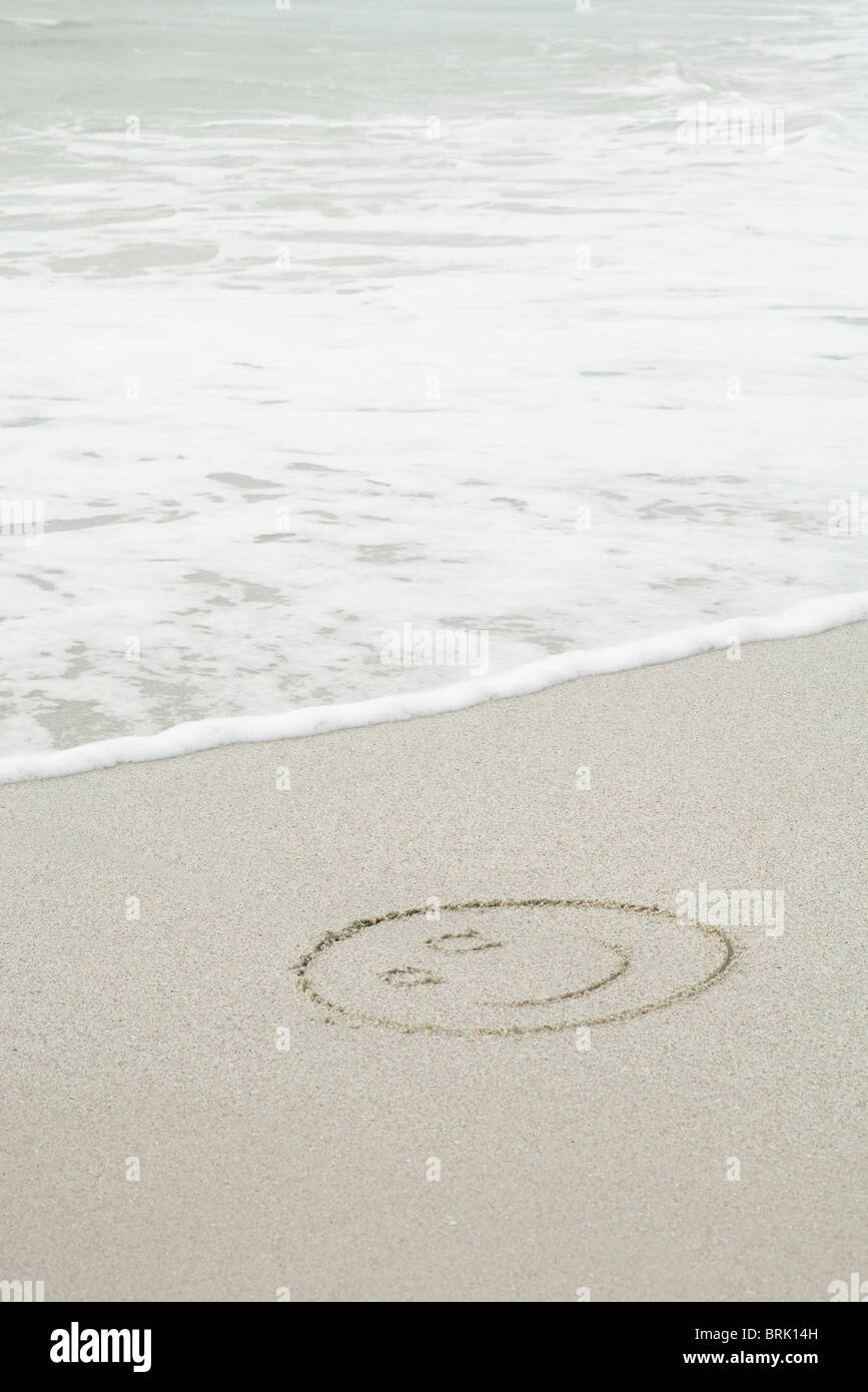Smiley dessiné dans le sable sur la plage Banque D'Images