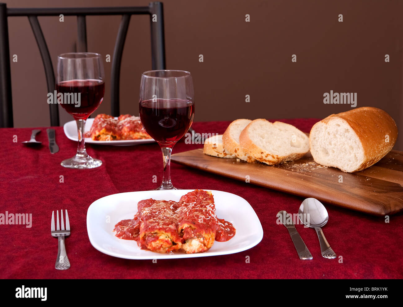 Deux plaques de manicotti farcis, un pain de tranches de pain italien et 2 verres de vin Banque D'Images