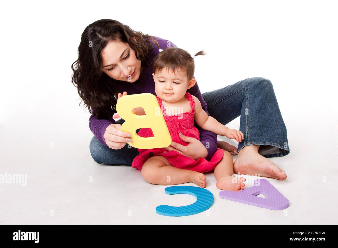 La mère, ou un enseignant heureux bébé à apprendre l'alphabet, A, B, C, avec des lettres de manière ludique, tout en étant assis sur le plancher. Banque D'Images