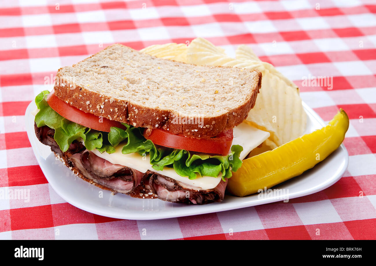 Un grand sandwich au rôti de bœuf sur pain d'avoine avec des tomates et de la laitue sur une assiette avec une nappe à carreaux rouges et blancs Banque D'Images