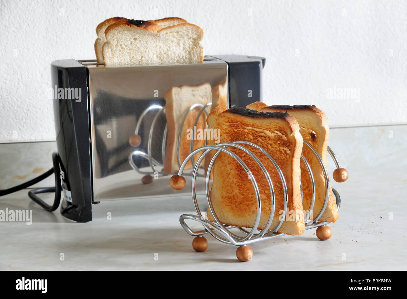 Du pain dans un grille-pain en acier inoxydable avec un toast rack avec des tranches de pain grillé assis devant elle. Banque D'Images