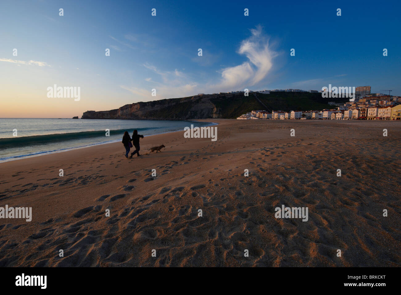 Un couple et leur chien marcher dans la plage au coucher du soleil à Nazaré, Portugal Banque D'Images