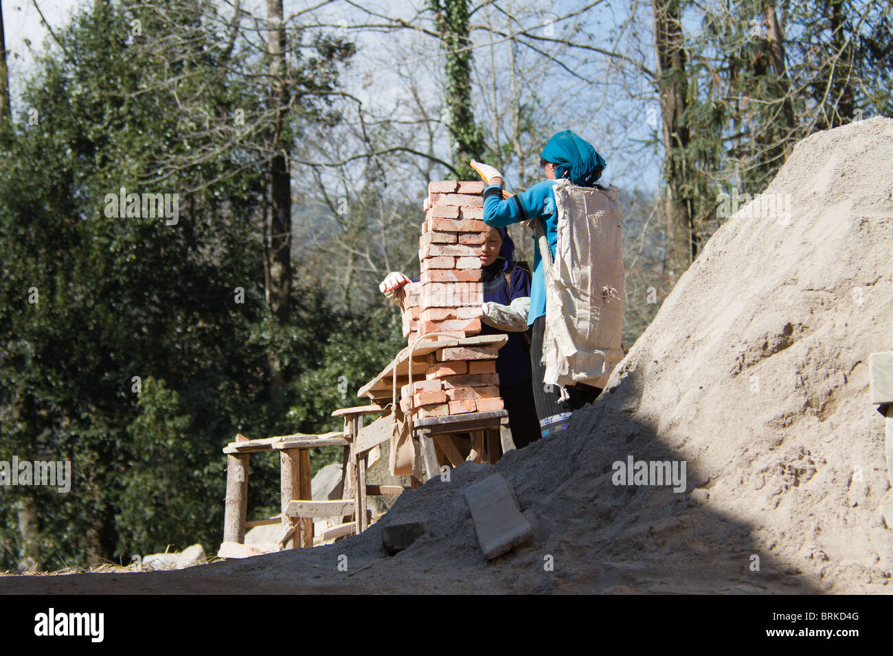 Une femme de la minorité chinoise se prépare à soulever et transporter une lourde charge de briques sur un chantier de construction. Banque D'Images