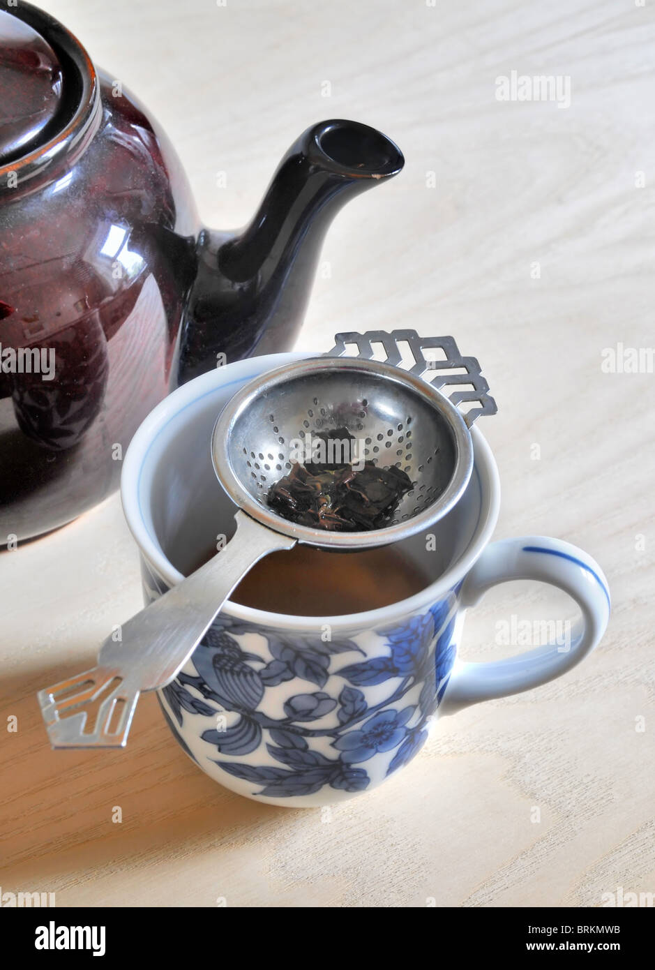 Une tasse de thé avec une passoire du thé et les feuilles de thé - assis à côté d'un pot de thé en céramique. Banque D'Images