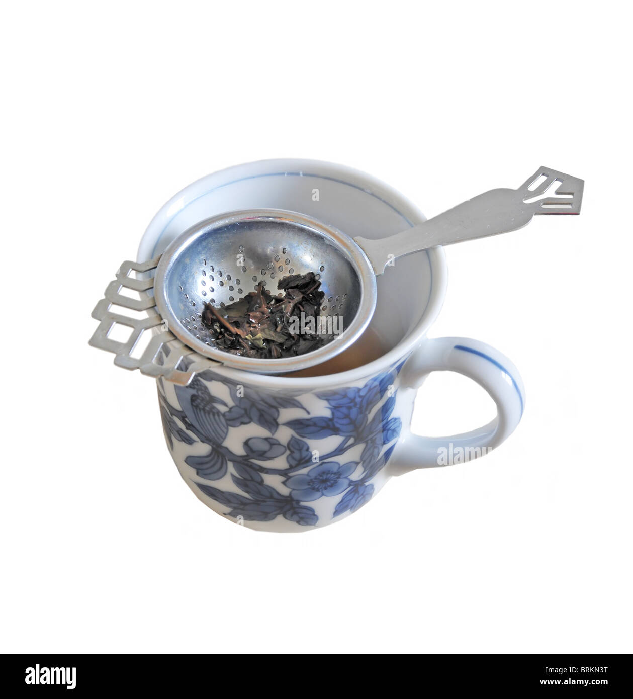 Une crépine de thé assis sur une tasse pleine de feuilles de thé. Banque D'Images