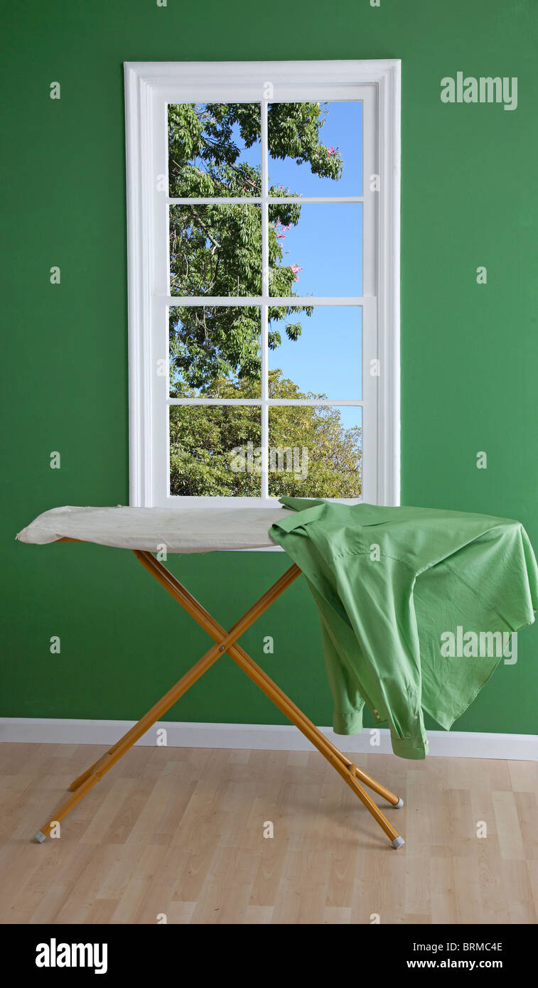 Planche à repasser avec chemise verte à côté de fenêtre Banque D'Images