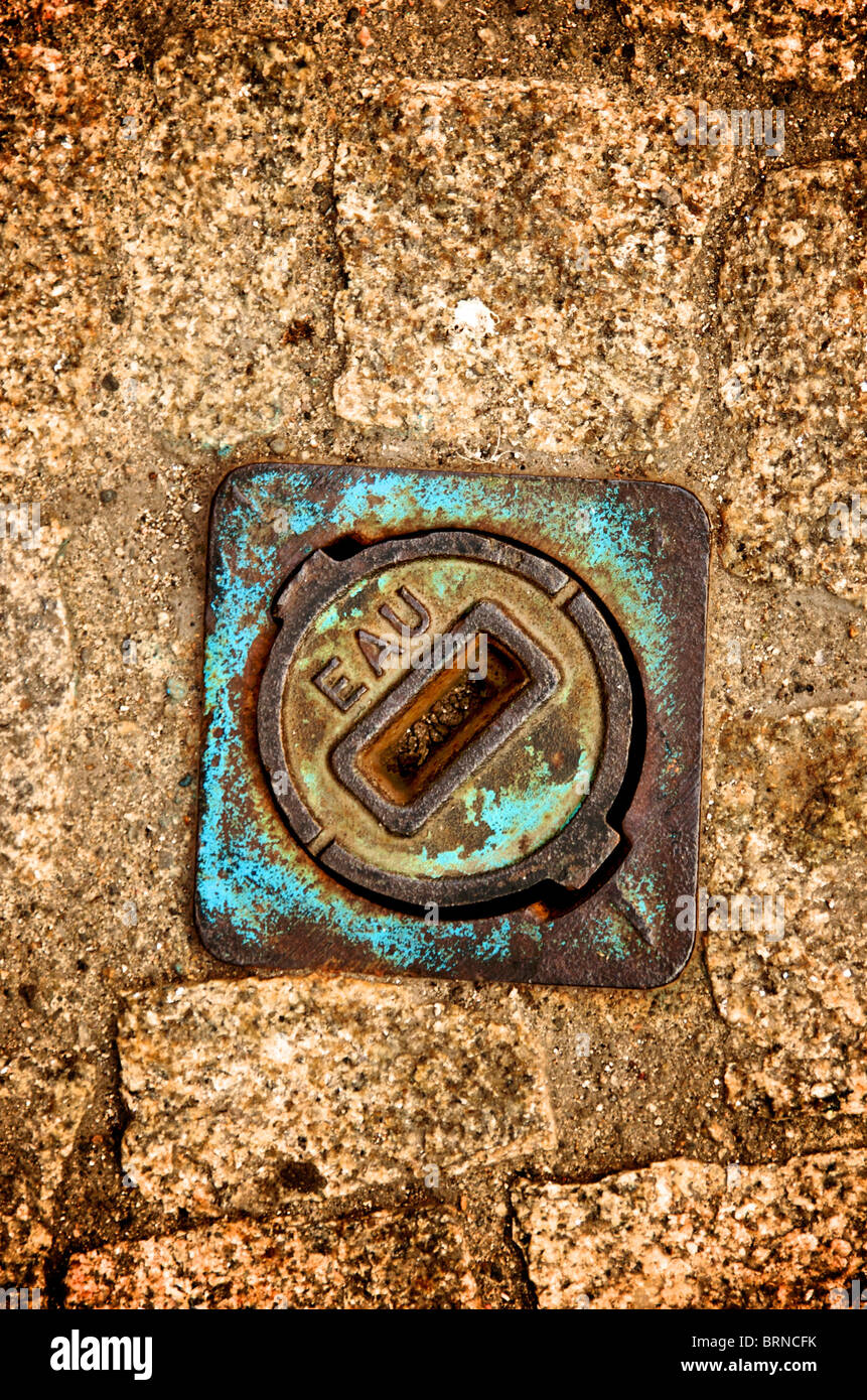 Détail urbain avec couvercle de trou d'homme en métal vintage reposant sur de la pierre altérée Banque D'Images