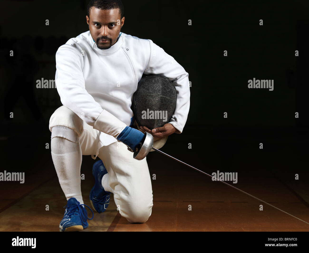 Portrait d'un tireur portant des uniformes d'escrime et de tenir une épée dans un gymnase sur fond noir Banque D'Images