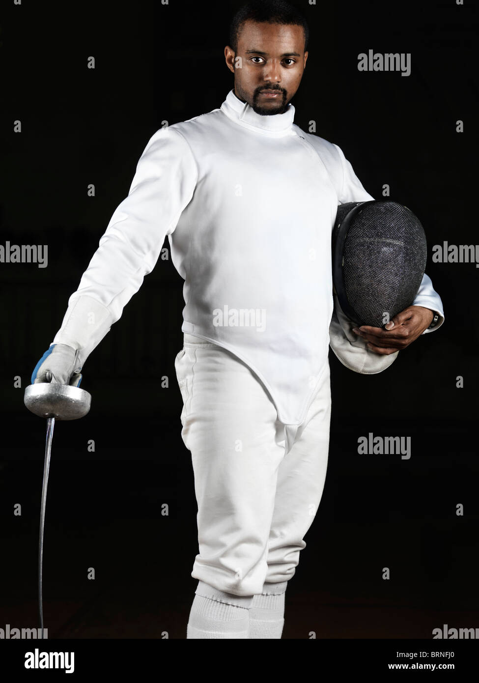 Portrait d'un tireur portant des uniformes d'escrime et de tenir une épée et un masque isolé sur fond noir Banque D'Images