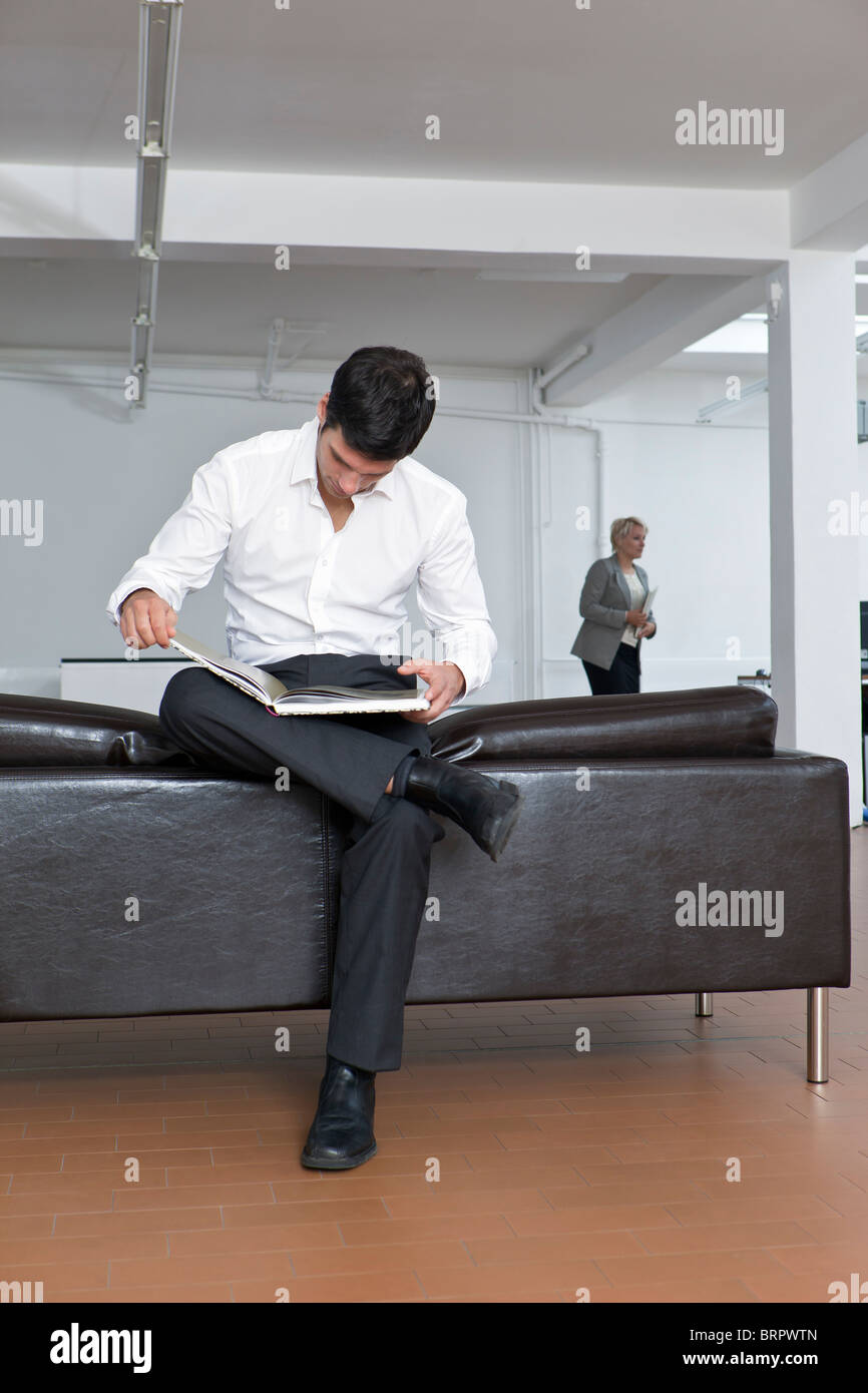 L'homme de l'examen d'un livre sur le canapé Banque D'Images