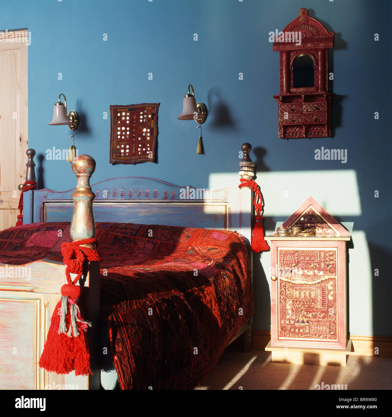 Glands rouge et de velours rouge lit de style indien-couvercle sur le lit peint en bleu chambre avec table de chevet de style indien Banque D'Images