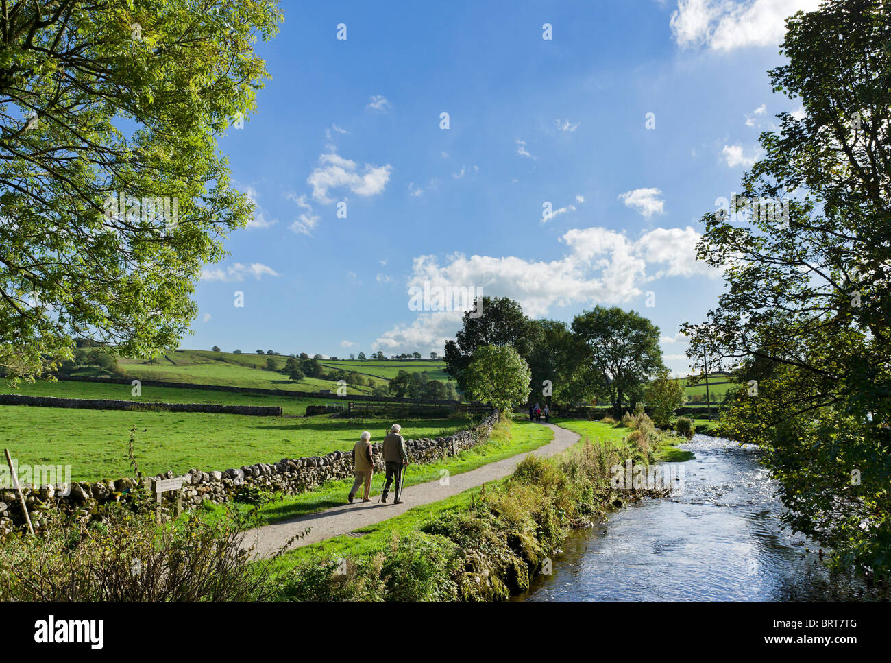Personnes âgées en train de marcher aux côtés de Malham Beck dans le village de Malham, Wharfedale, Yorkshire Dales National Park, England, UK Banque D'Images