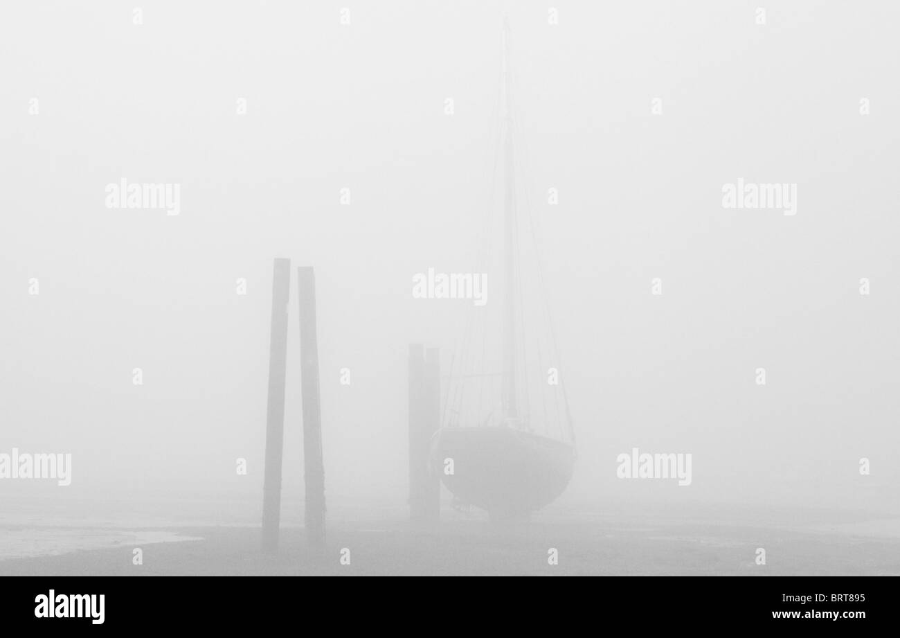 Un bateau amarré à marée basse dans le brouillard, à West Mersea Banque D'Images