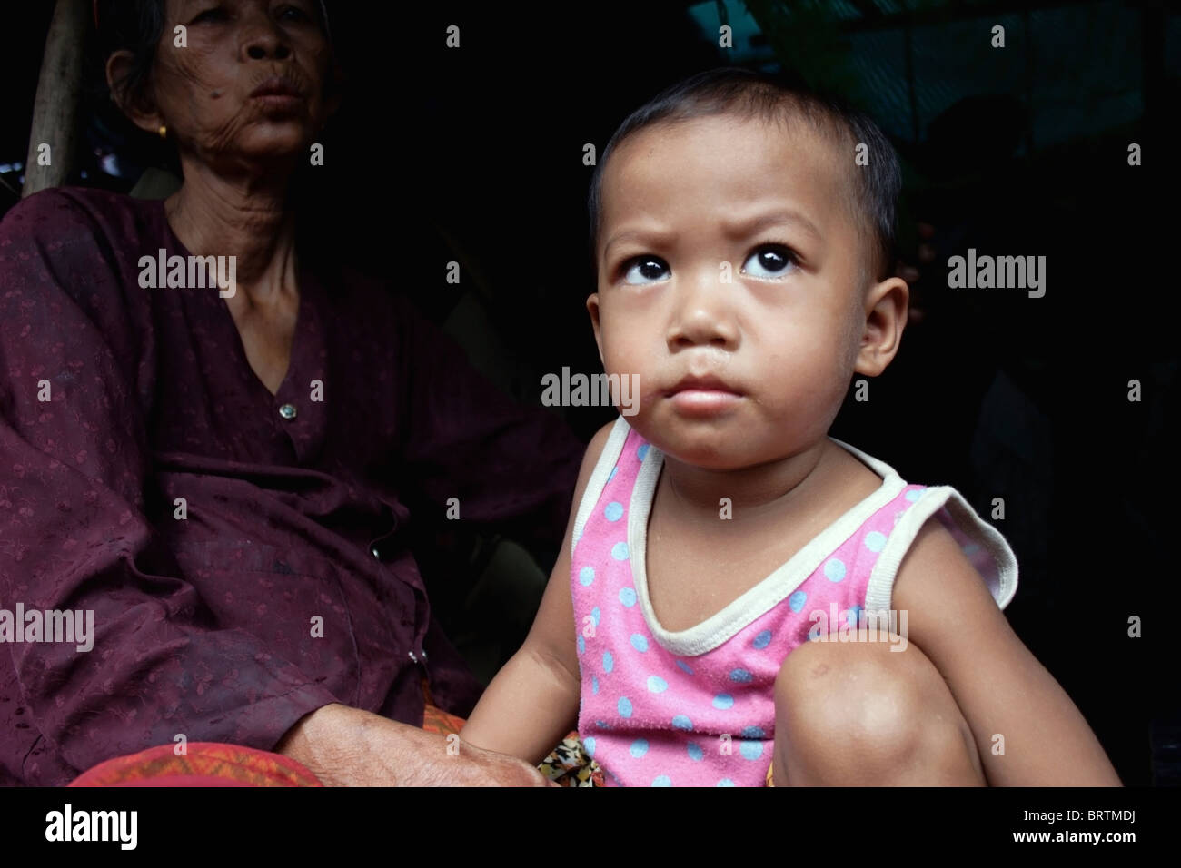 Un bébé vivant dans la pauvreté est à la recherche d'un porche d'une maison dans un bidonville de squatteurs situé dans une ruelle à Phnom Penh, Cambodge. Banque D'Images