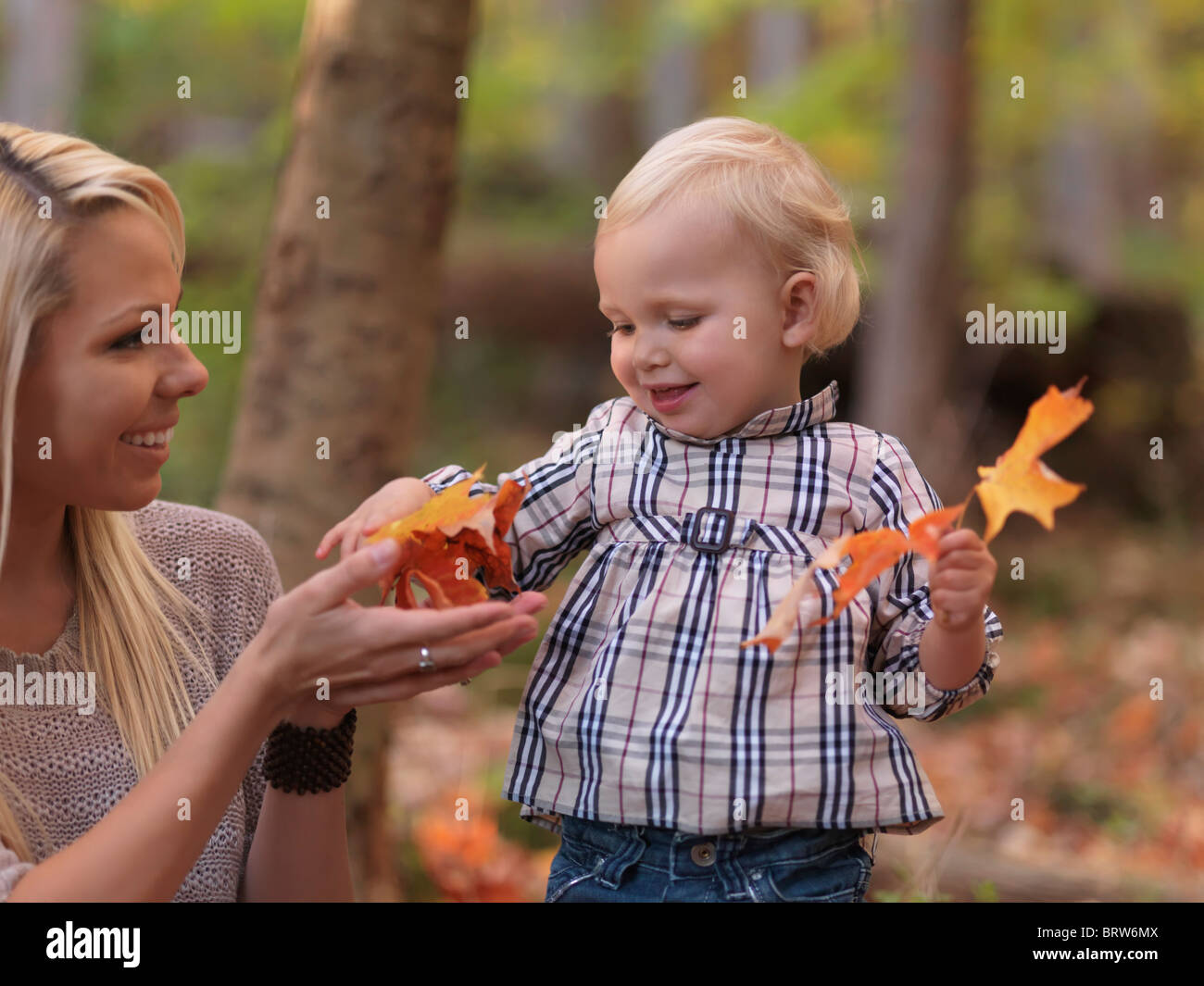 Heureux fillette de deux ans et sa mère l'automne les feuilles tombées de rassemblement dans un parc Banque D'Images