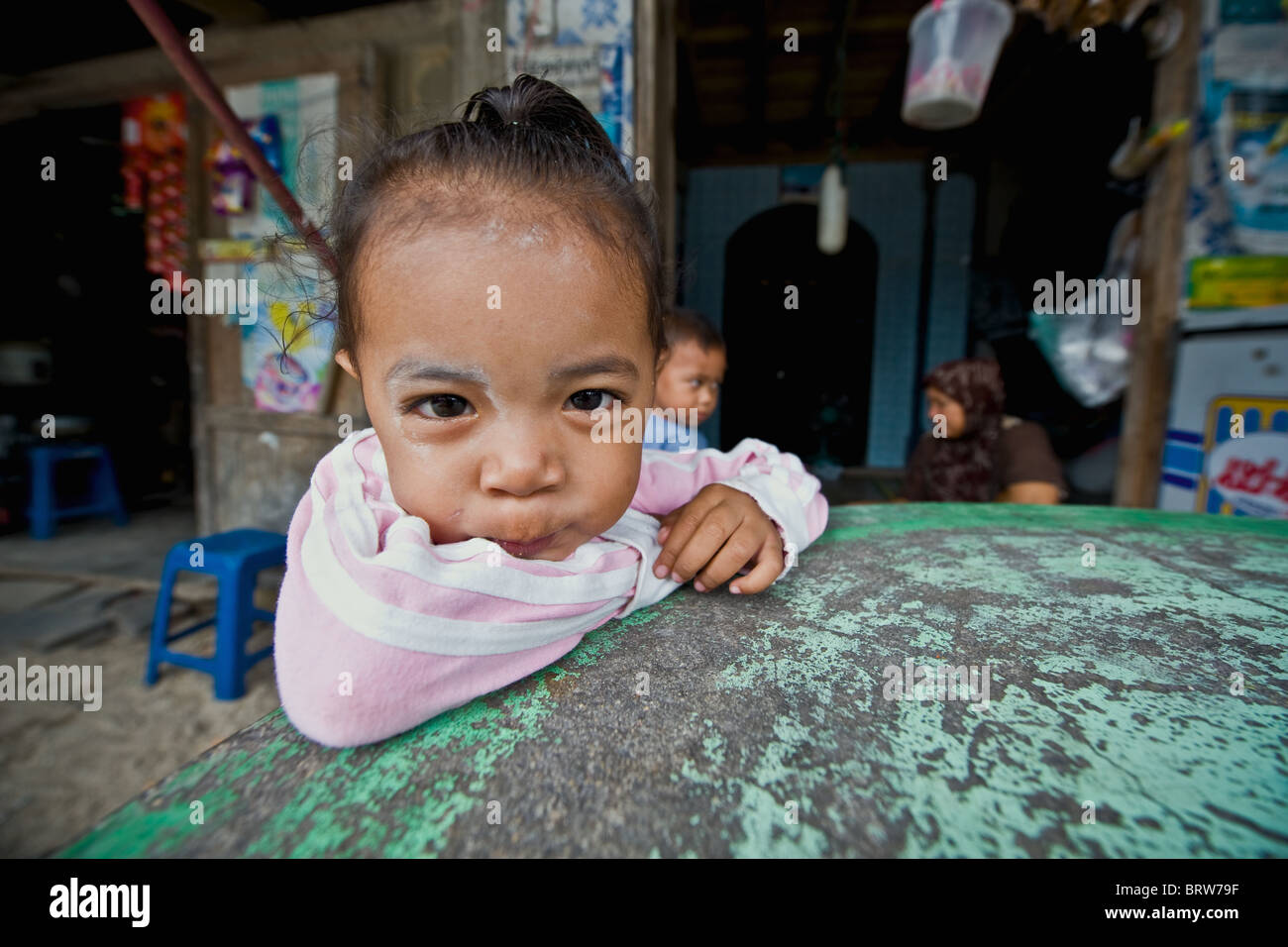 Jeune fille regarde la caméra, tandis que son frère et sa mère s'asseoir à l'arrière-plan. Ban Hau Thanon, Koh Samui. Thaïlande Banque D'Images