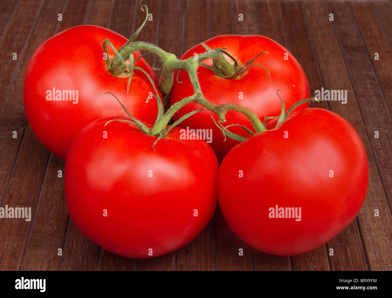 Vigne quatre tomates mûres sur un mat en bois brun Banque D'Images
