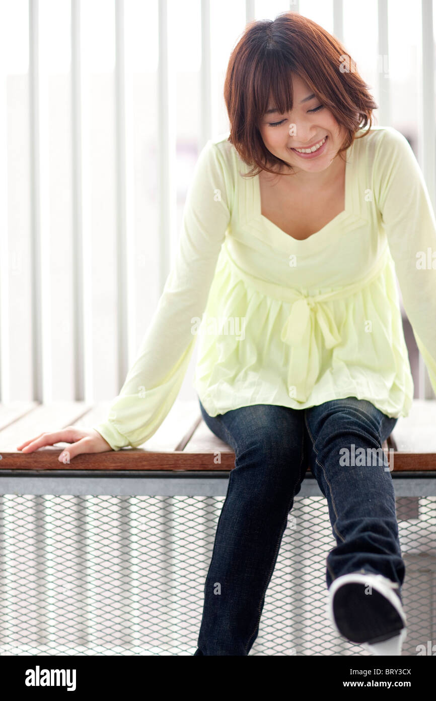 Jeune femme assise sur un banc, smiling Banque D'Images