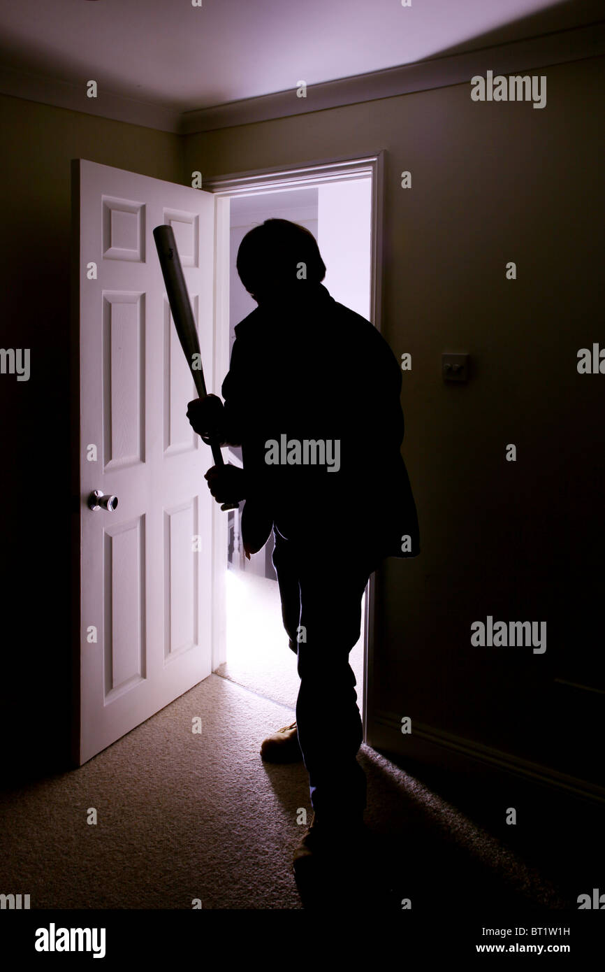 Silhouette masculine figure entre dans une pièce sombre avec une batte de baseball Banque D'Images