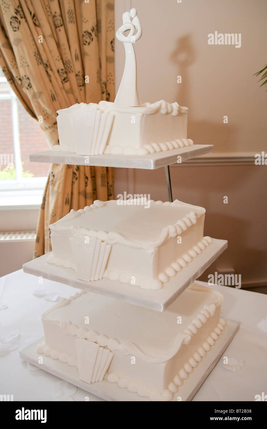 Un gâteau de mariage blanc à trois niveaux de style Art déco des années 1930 exposé lors d'une réception de mariage, avec des détails de glaçage et un haut moderne pour mariée et mariée Banque D'Images
