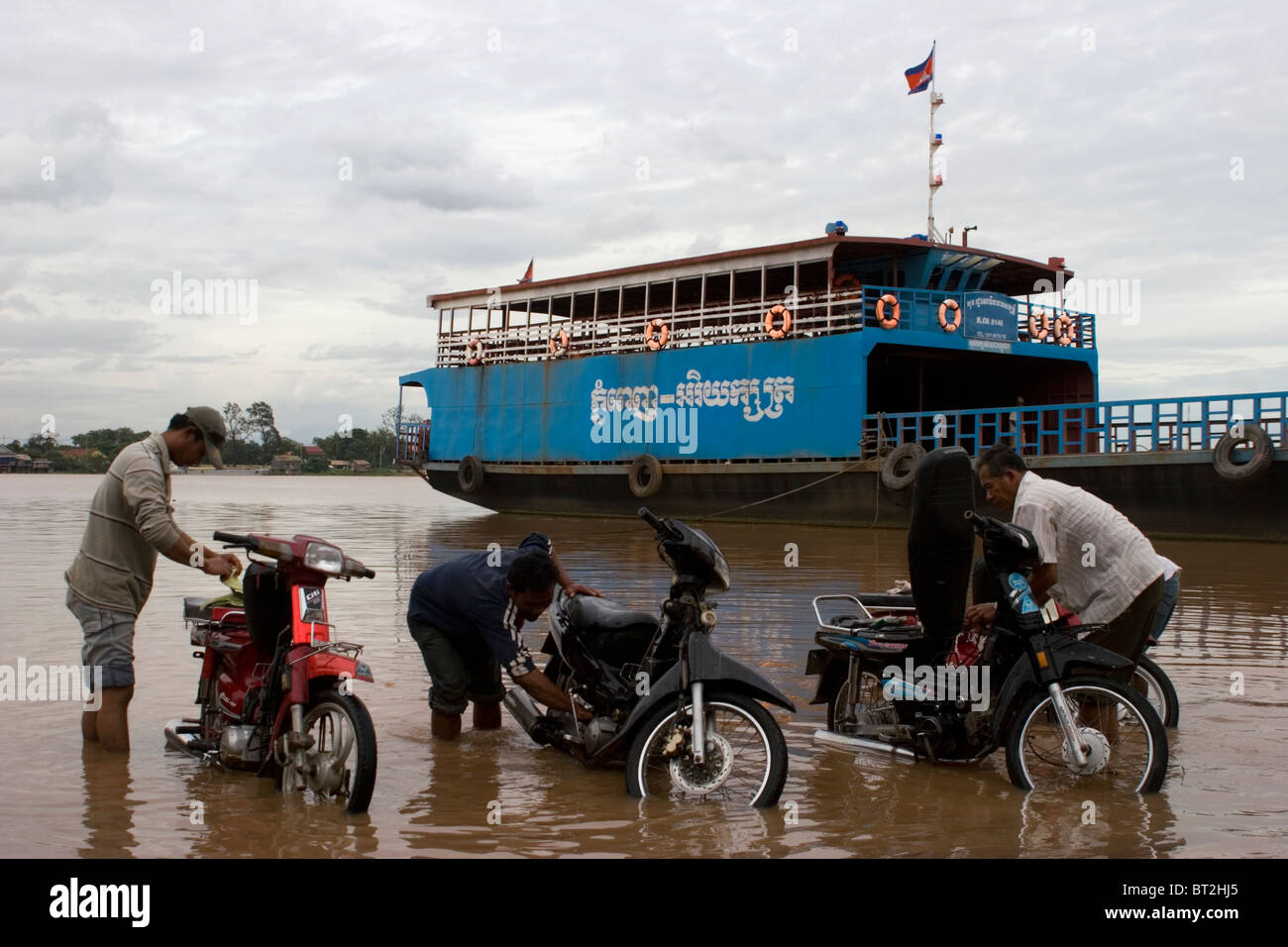 Un groupe de chauffeurs de taxi moto lavent leur voiture à la muddy Mékong à Phnom Penh, Cambodge. Banque D'Images