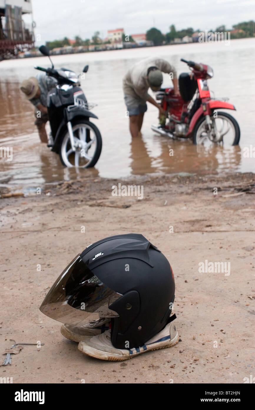 Un casque de moto est sur le dessus d'une paire de chaussures boueuses près du Mékong à Phnom Penh, Cambodge. Banque D'Images