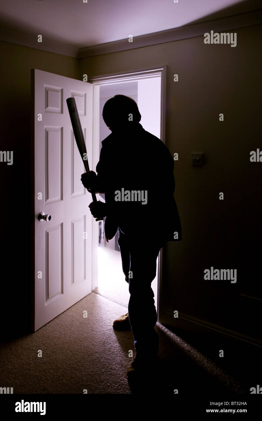 Silhouette masculine entre dans une pièce sombre avec une batte de baseball Banque D'Images