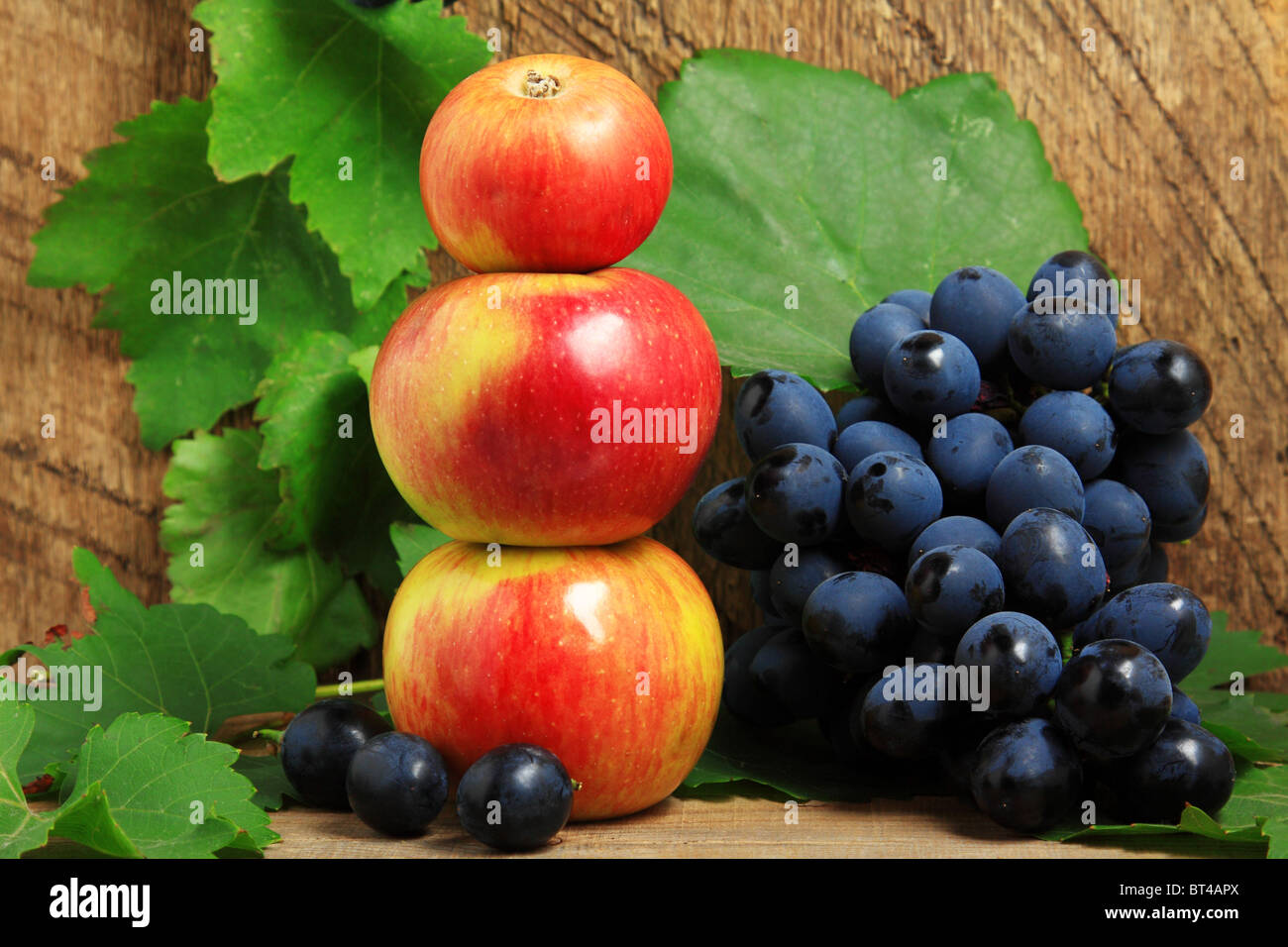 Trois pommes et grappe de raisins sur fond de bois Banque D'Images