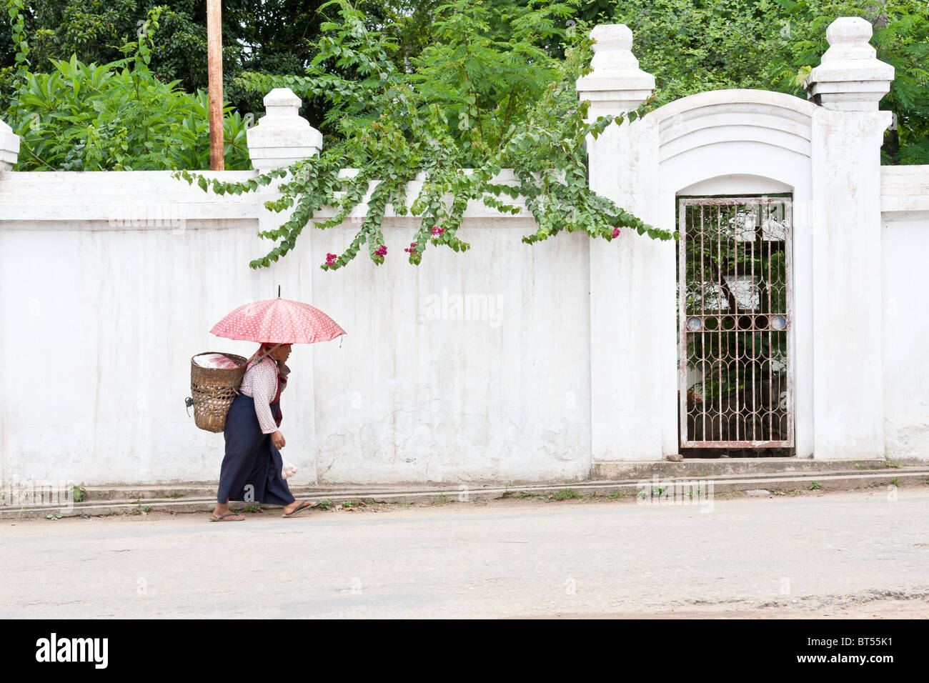 Une minorité de femme portant des fleurs qu'elle a acheté au marché du matin dans la région de Keng Tong, le Myanmar passe devant un mur blanc sur son chemin du retour Banque D'Images