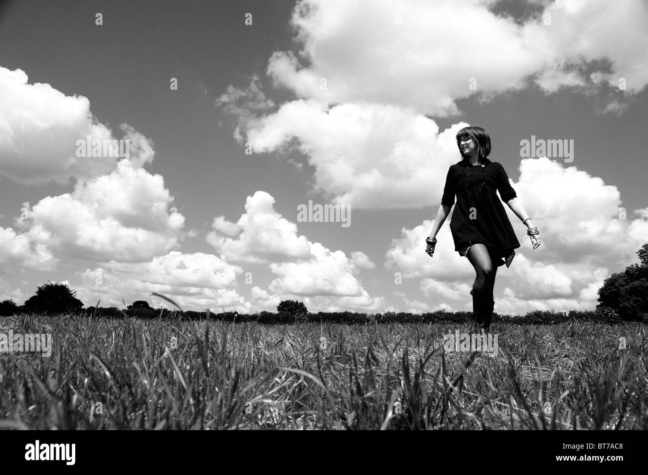 Marcher dans un champ, une jeune femme marche dans le soleil d'été avec des nuages derrière. Banque D'Images