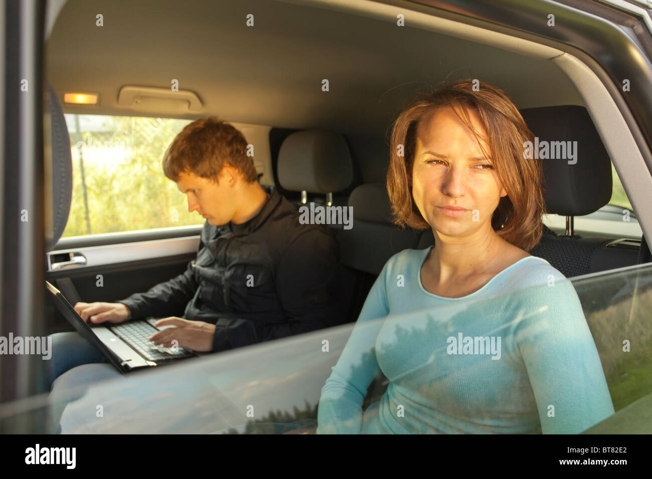 Femme regarde soigneusement hors de la fenêtre de la voiture tandis que l'homme à côté de son travail sur ordinateur portable dans le siège arrière Banque D'Images