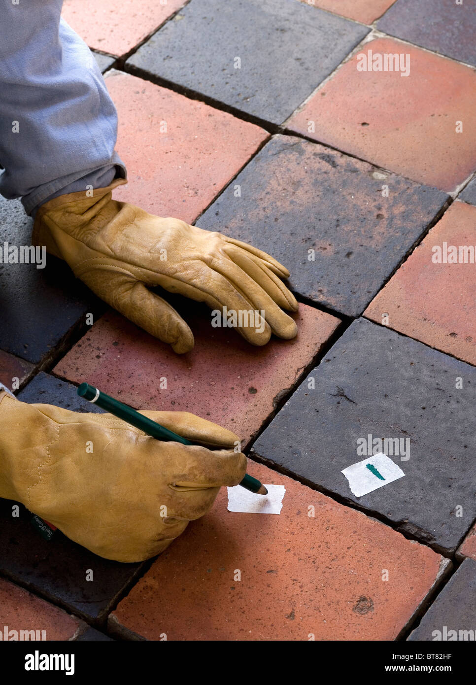 Close-up de mains dans des gants sur le vieux noir +carrelage terre cuite quarry Banque D'Images