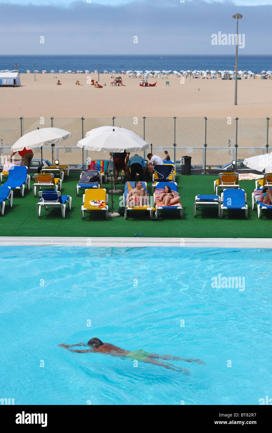 L'homme nage par un groupe de personnes de soleil à côté d'une piscine extérieure en face de la plage de Figueira da Foz Banque D'Images