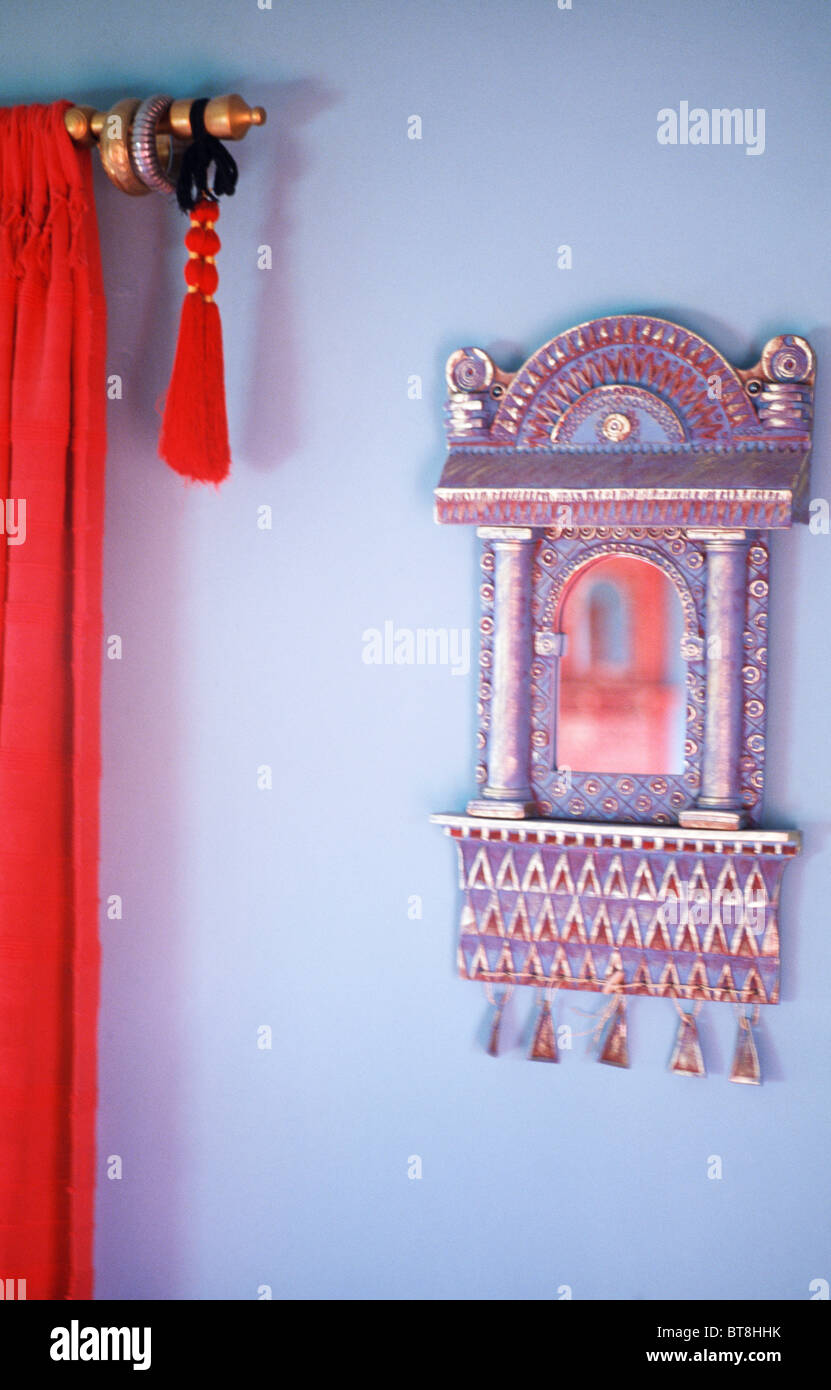 Close-up of ornate miroir de style indien à côté du rideau rouge avec pompon sur mur mauve Banque D'Images