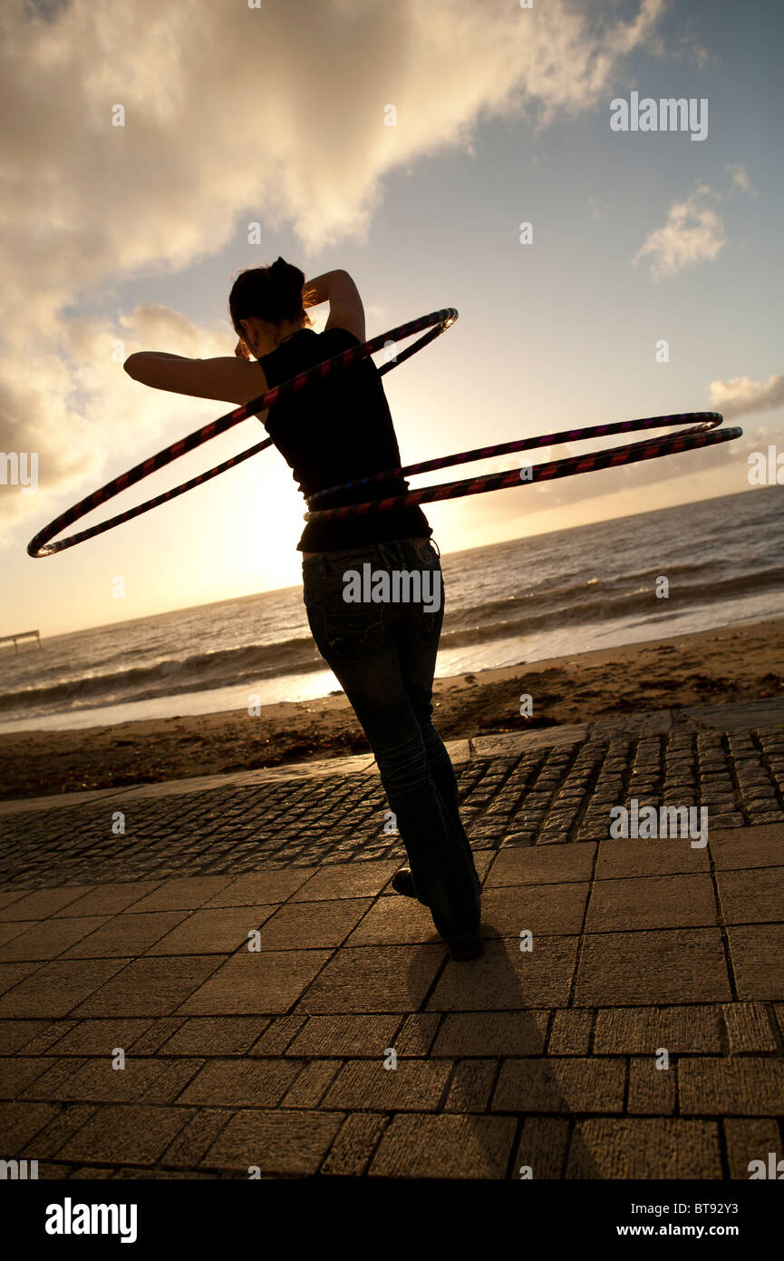 Une jeune femme étudiant à l'université d'Aberystwyth en utilisant hoolah ou hula hoops au coucher du soleil, UK Banque D'Images