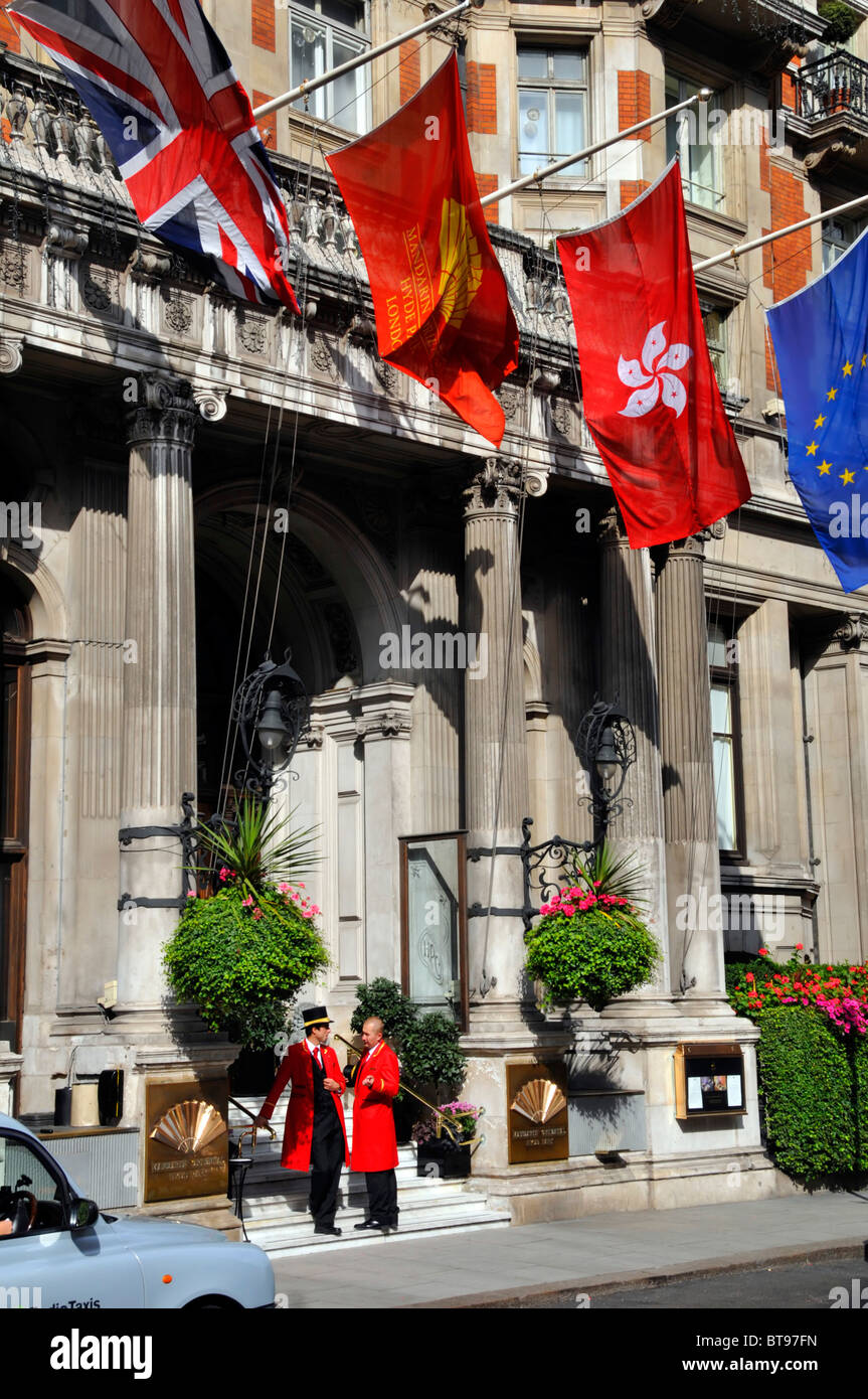 Drapeaux au-dessus de deux portiers à l'entrée du luxe Hôtel cinq étoiles Mandarin Oriental Hyde Park à London Knightsbridge Taxi britannique en Angleterre en attente Banque D'Images