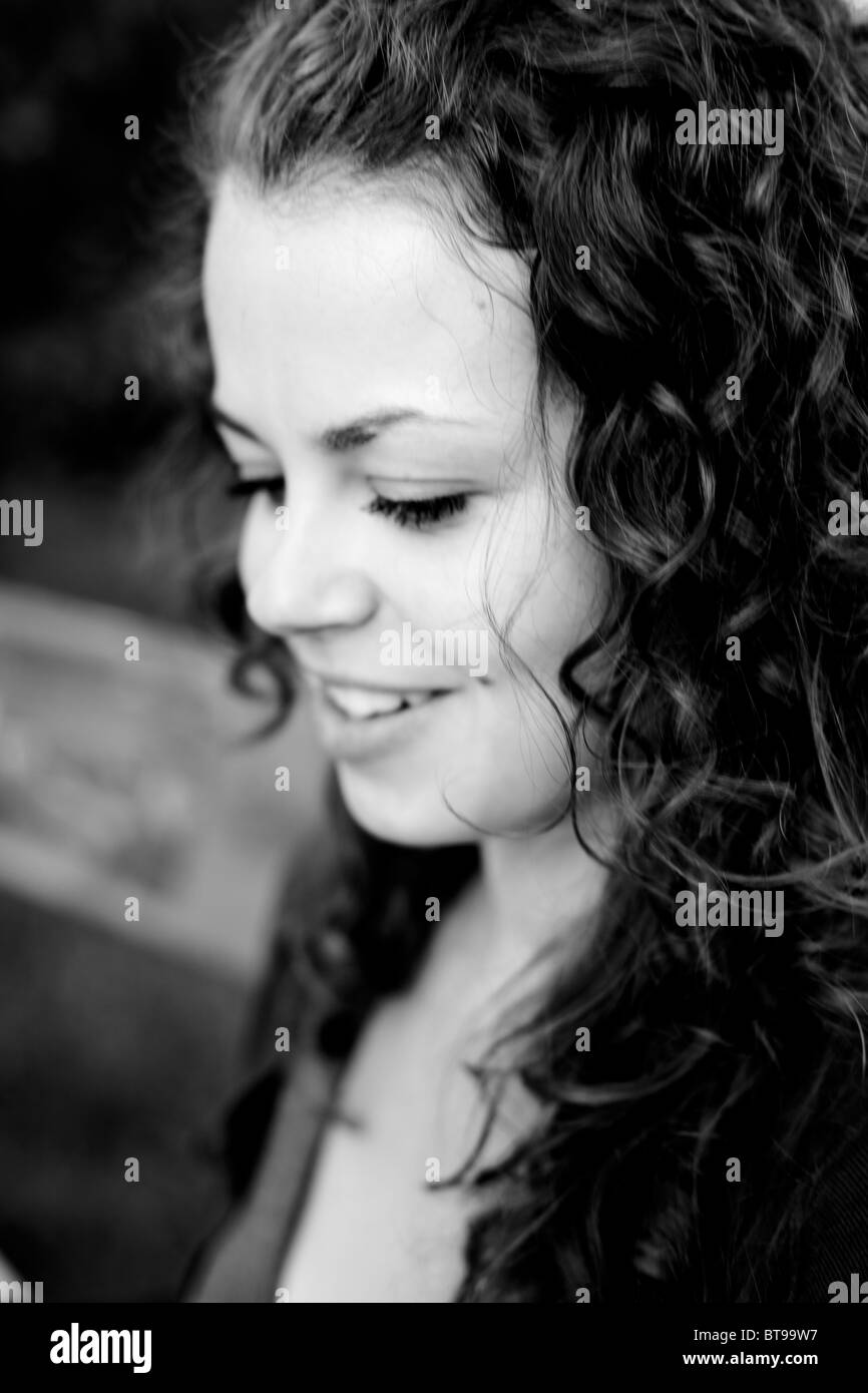 Jeune femme souriante avec les cheveux bouclés regardant vers le bas, gros plan extérieur noir et blanc Banque D'Images