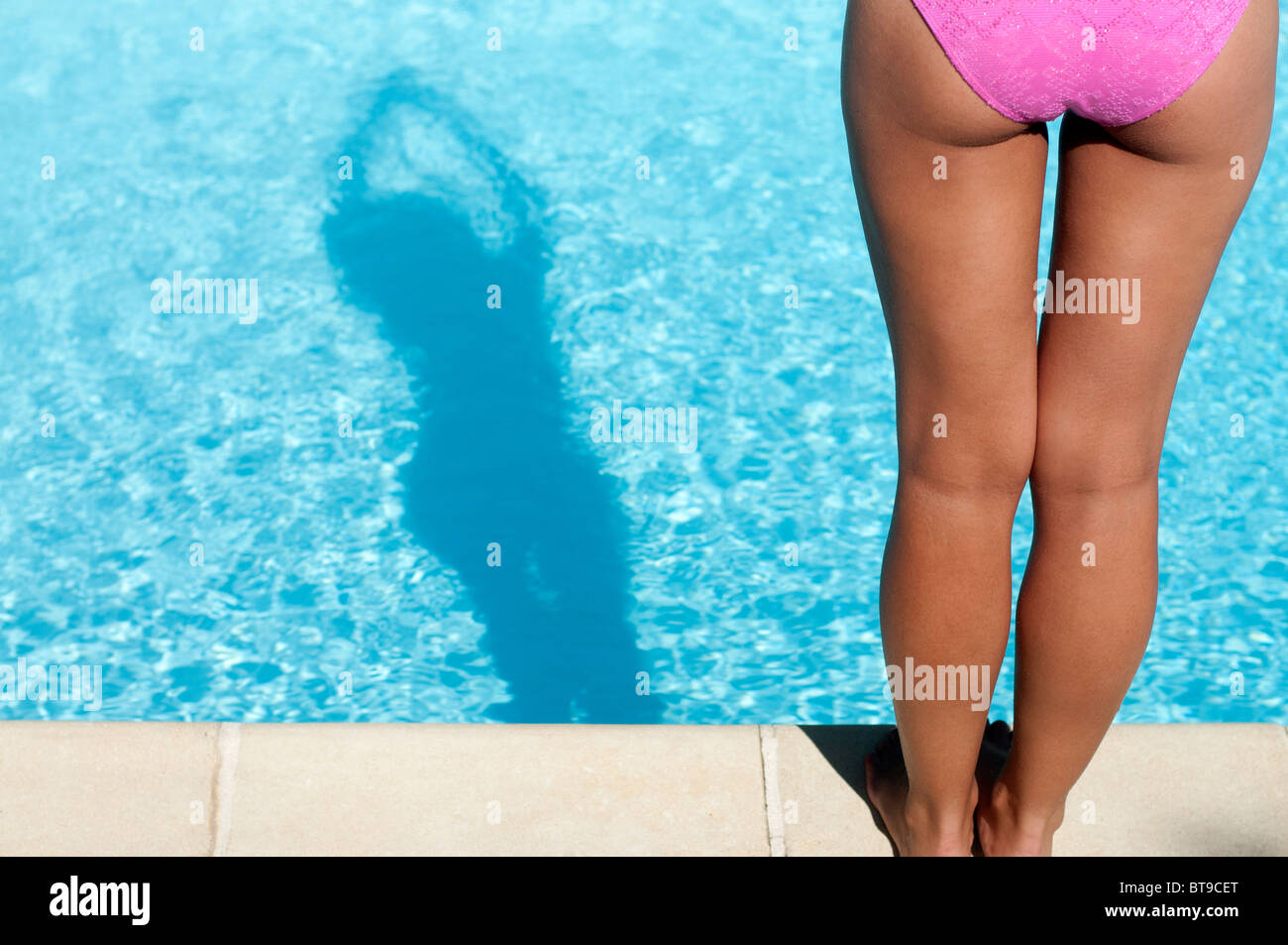 Une jeune femme en bikini rose debout au bord d'une piscine, vue arrière Banque D'Images
