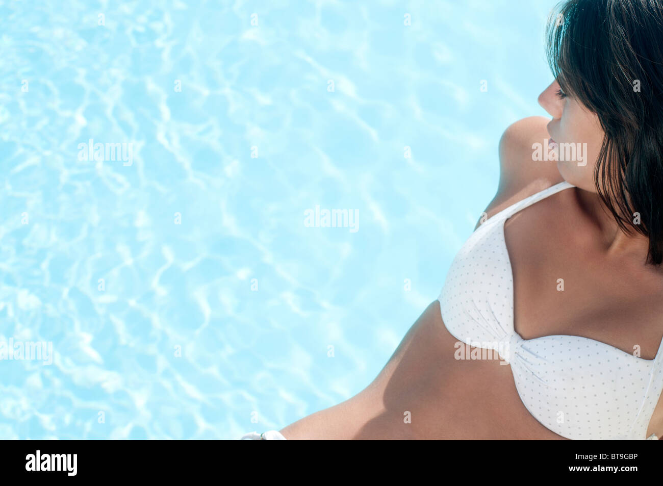 Une jeune femme en bikini blanc assis au bord d'une piscine Banque D'Images