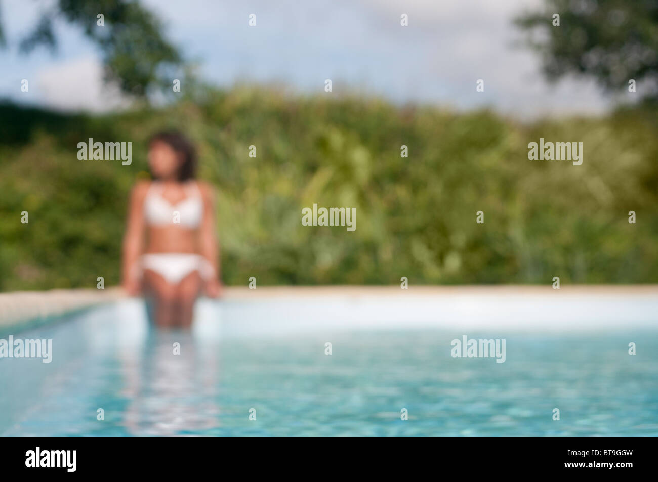 Une femme assise à une piscine extérieure, des jambes dans l'eau Banque D'Images