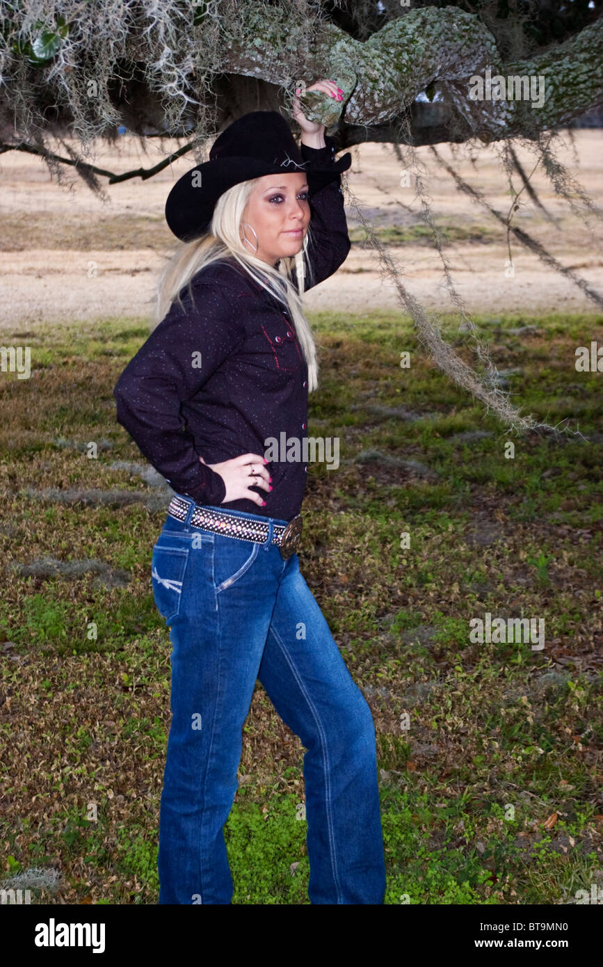 Belle jeune cowgirl au début de la vingtaine, avec de longs cheveux blonds qui coule, posant sous big Oak tree Banque D'Images
