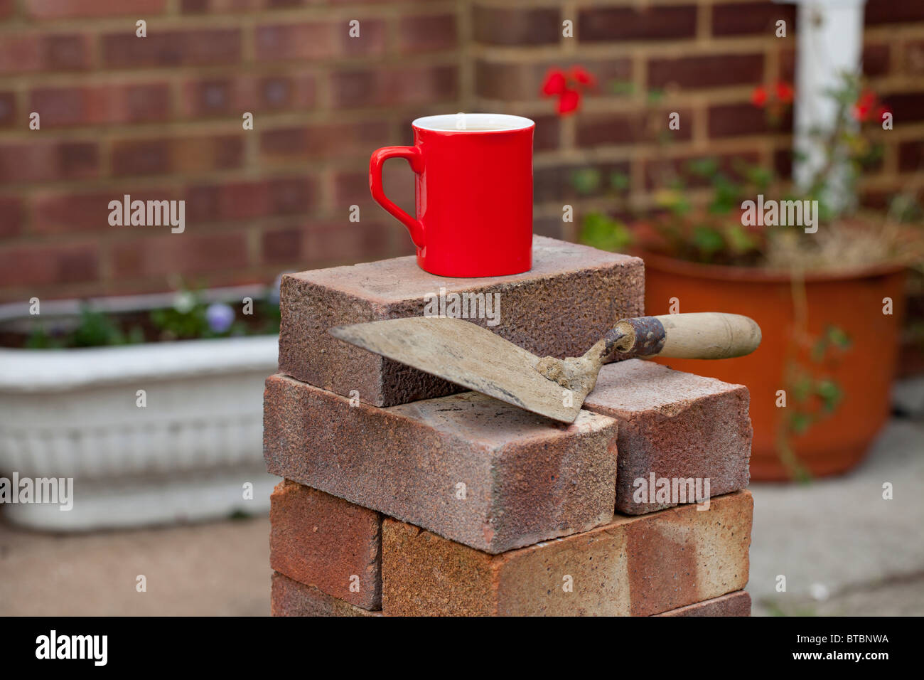 Maison d'une pile de briques avec une truelle, et de garder le constructeur heureux il y a une tasse de thé chaud. Banque D'Images